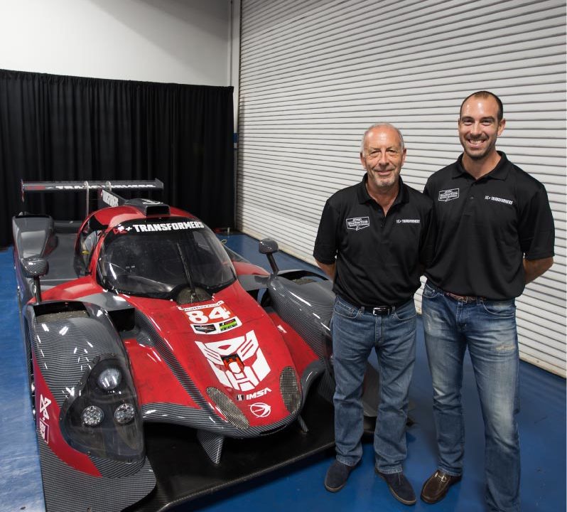Two men standing next to a race car.