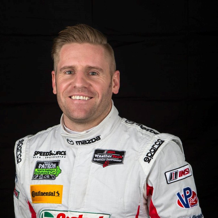 A man in white racing suit smiling for the camera.