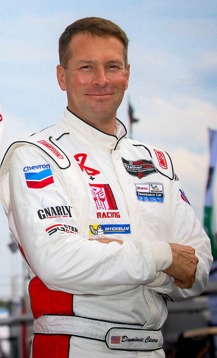 A man in white racing suit standing with his arms crossed.